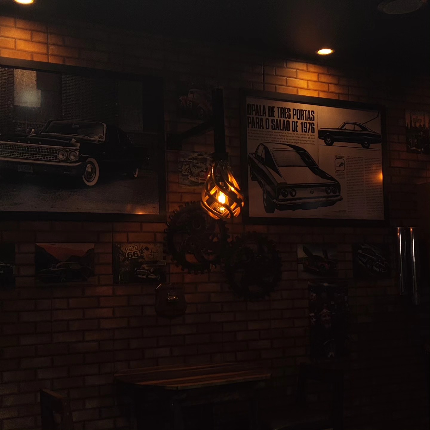 Decoração da barbearia com carros clássicos, engrenagens e parede de tijolos.